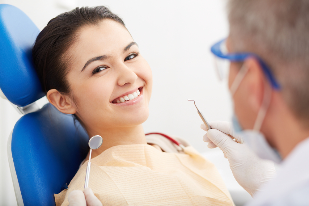 A woman smiling while being treated by a dentist - dental crown